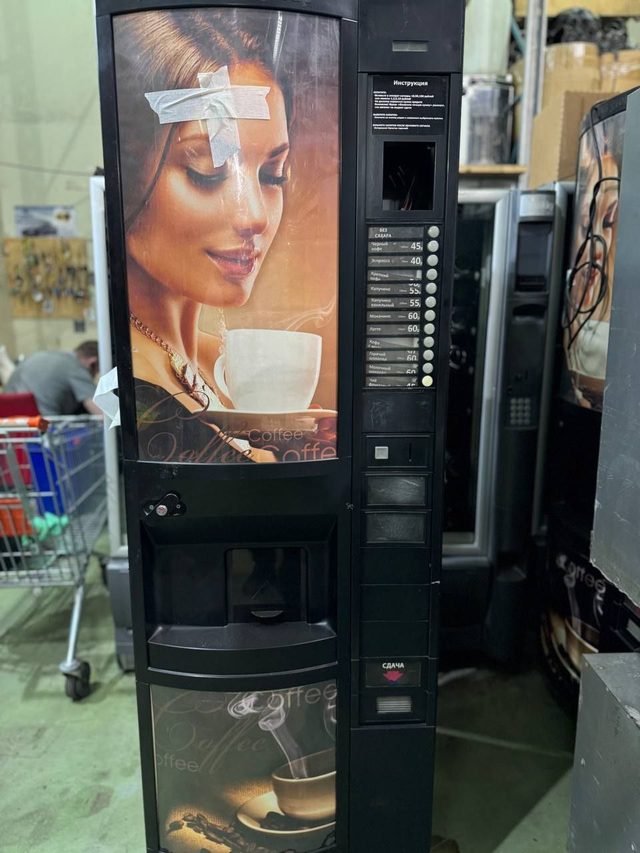 Кофейный автомат с рекламной картинкой, на картинке скотч, сзади склад