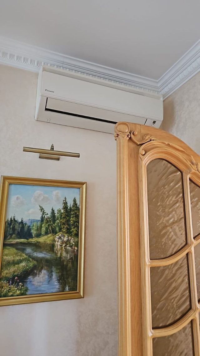 Внутренний блок кондиционера под потолком, рядом дверь и картина на стене